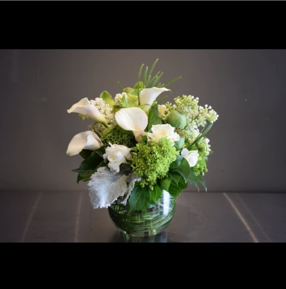 White calla lilies and green-white flowers in a glass vase