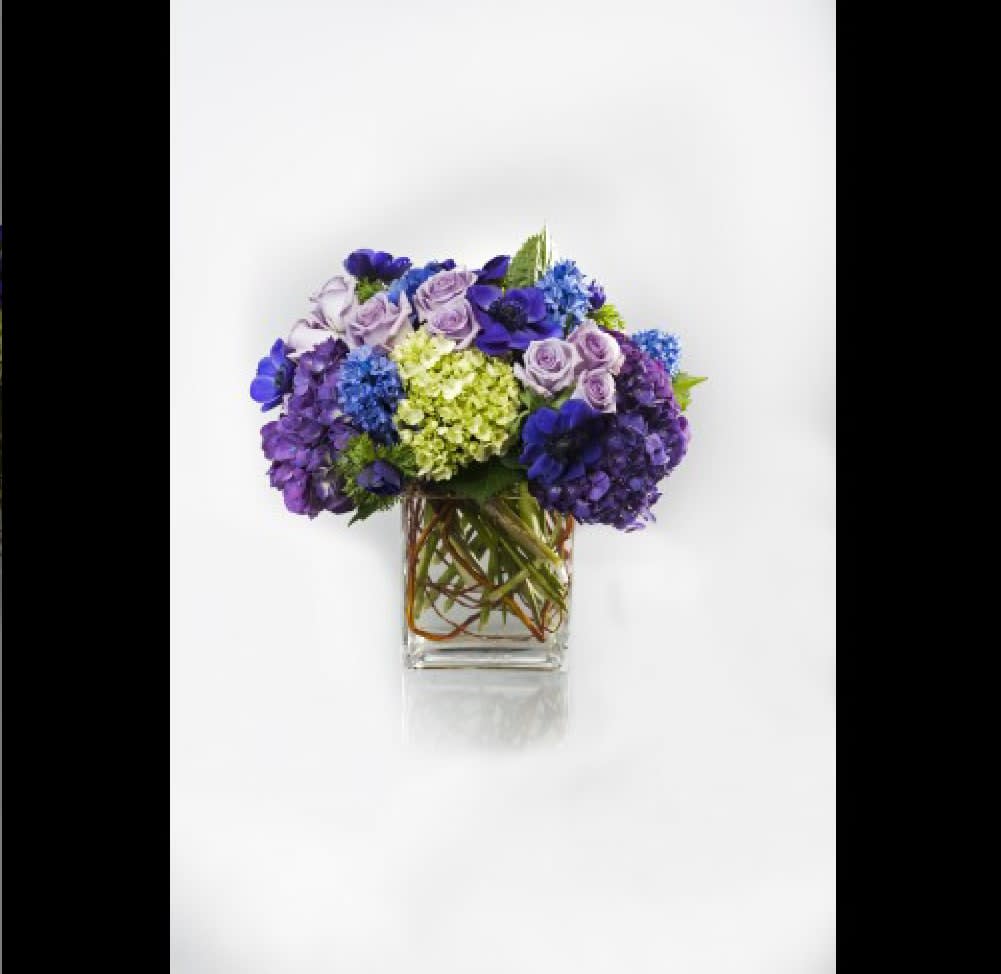 Purple and blue flower arrangement in a clear square vase