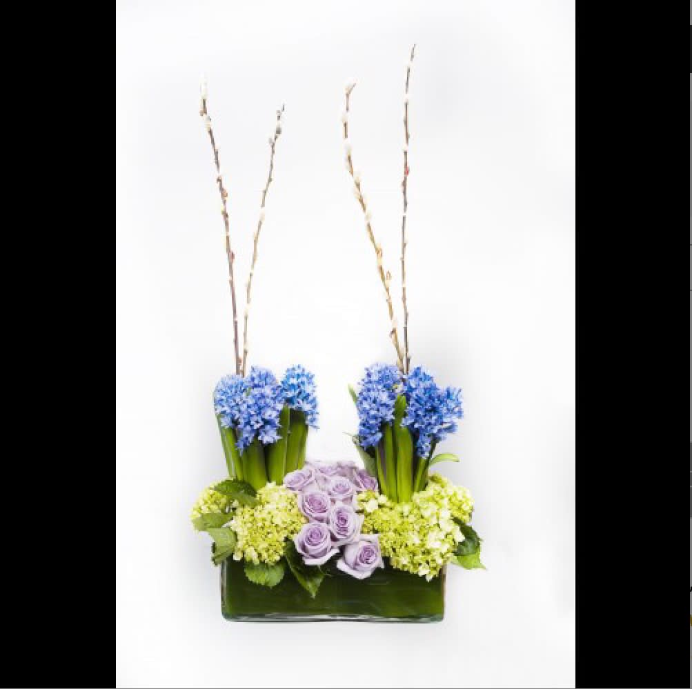 Blue and lavender flowers arranged in a rectangular vase with tall branches