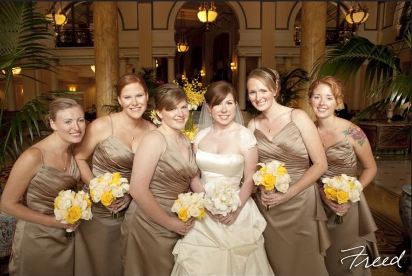 Bride and bridesmaids holding white and yellow bouquets indoors