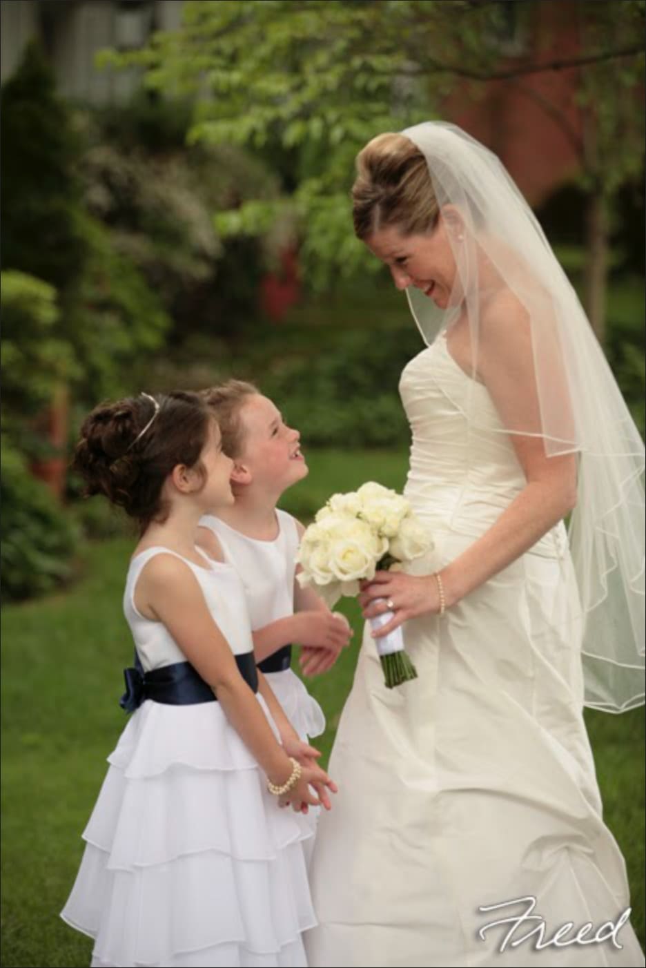 Bride in a white dress holding a white bouquet beside two flower girls