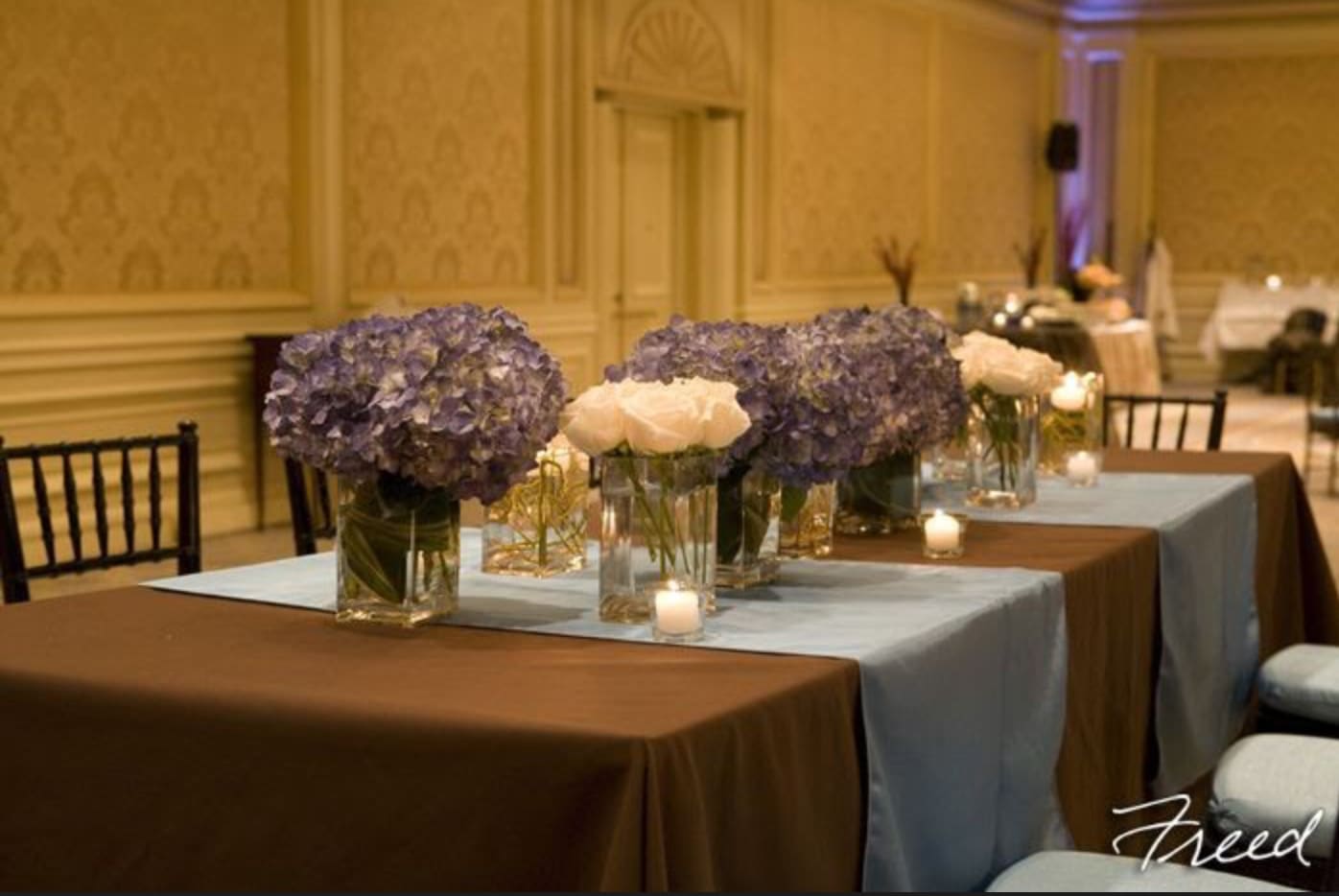 Purple hydrangea and white rose centerpieces in glass vases on a banquet table