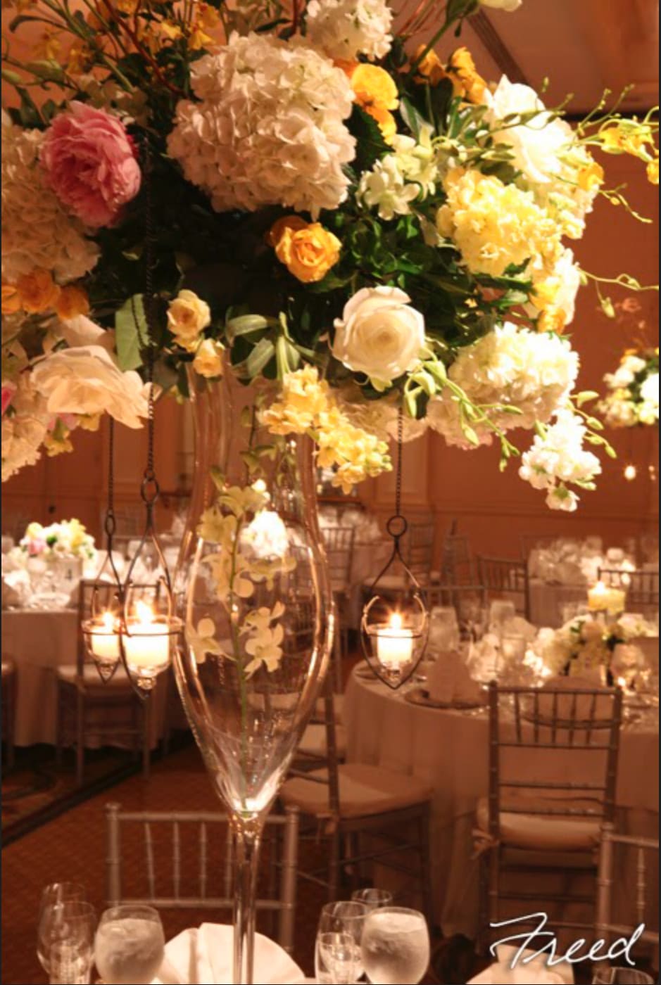 Tall floral centerpiece in a clear glass vase with hanging candle holders