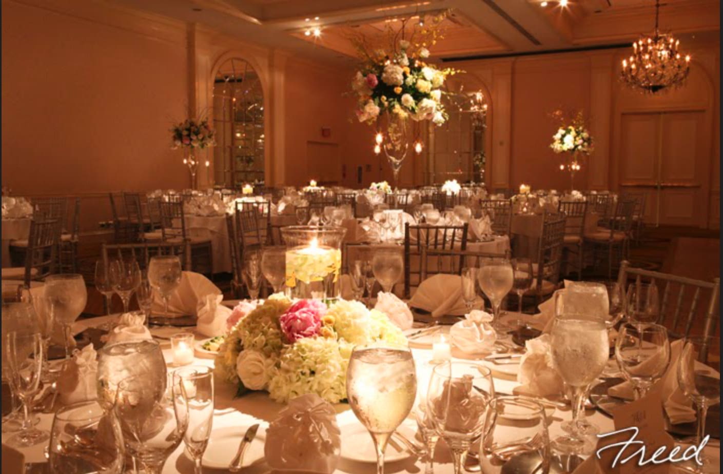 Floral centerpieces on round banquet tables in a warmly lit ballroom