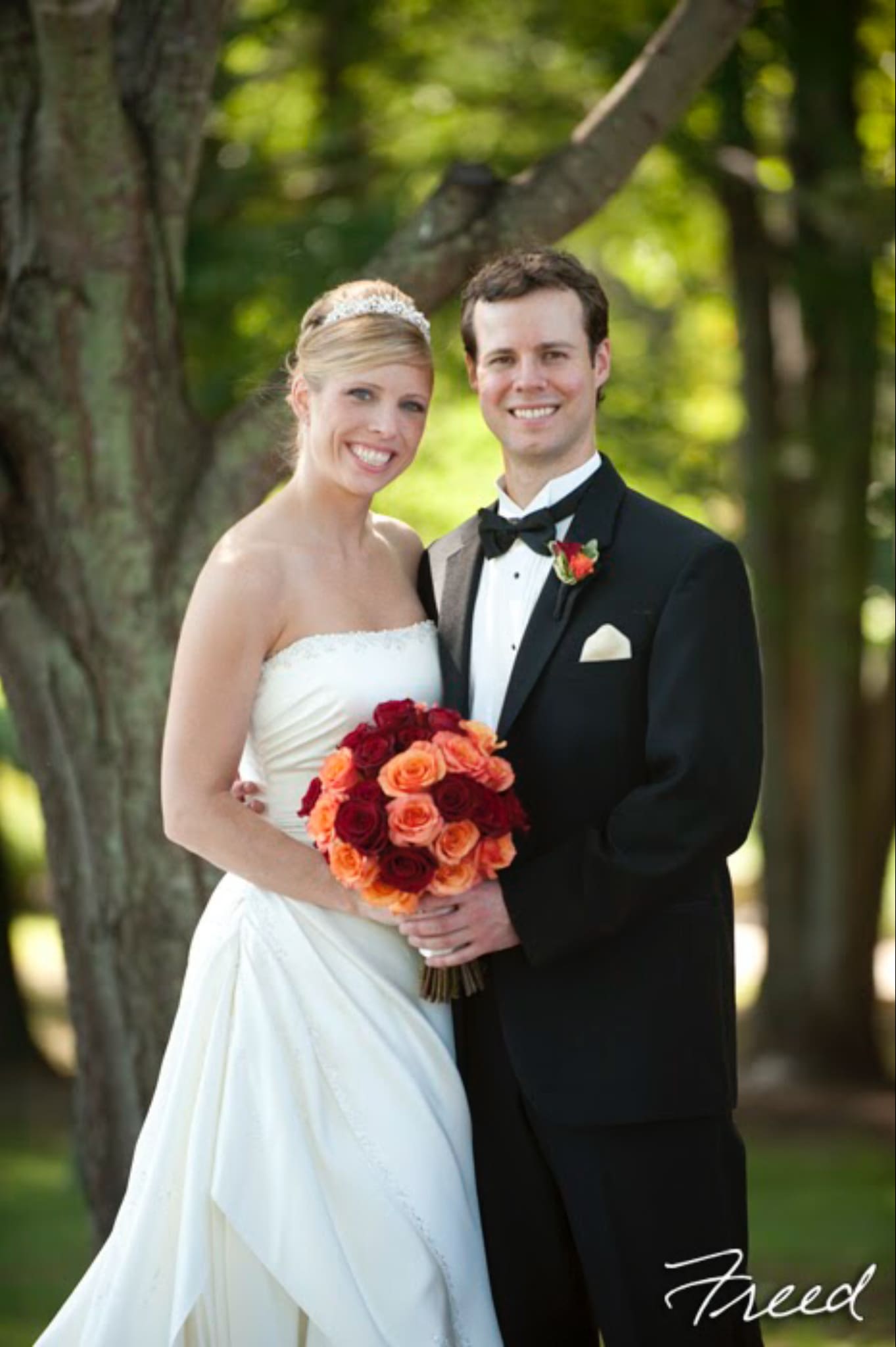 Bride and groom holding a bouquet of red and orange roses