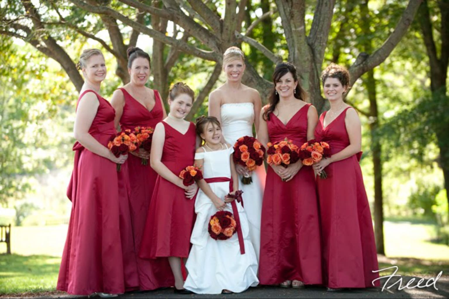 Bridal party in red dresses holding orange and burgundy bouquets
