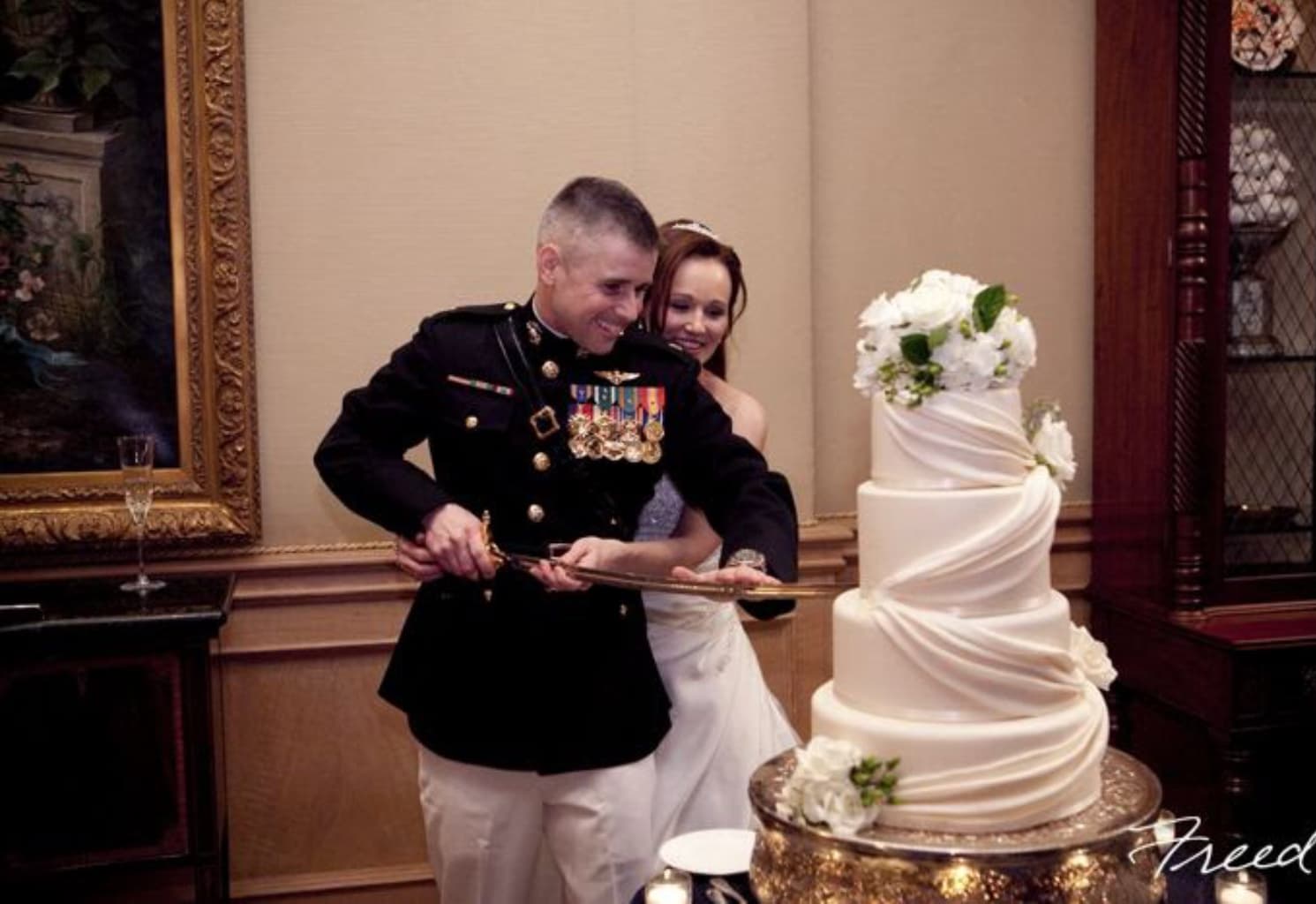 Bride and groom cutting a tall white wedding cake with white flowers
