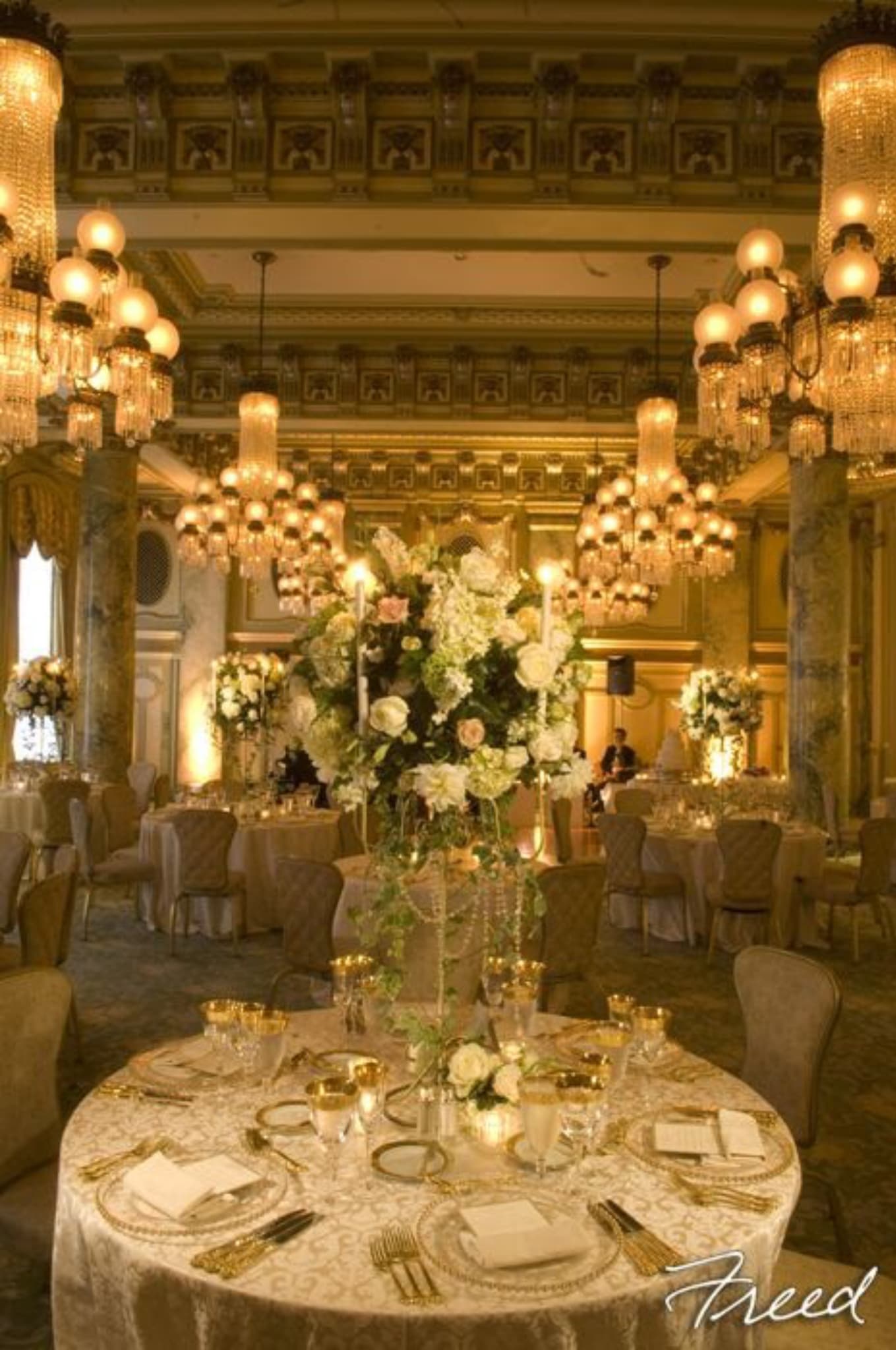 Elegant banquet hall with tall white floral centerpieces and gold table settings