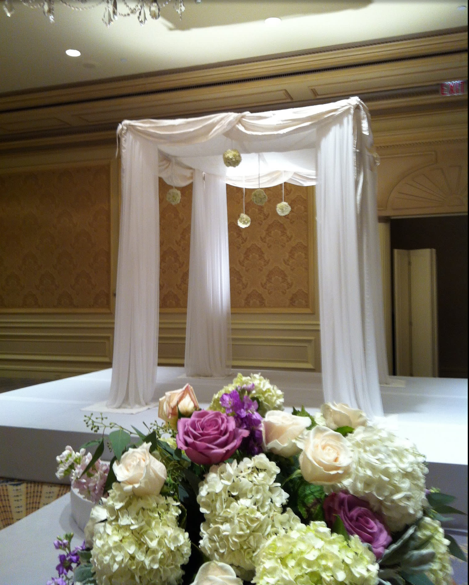 Purple and cream rose arrangement in front of a white draped canopy