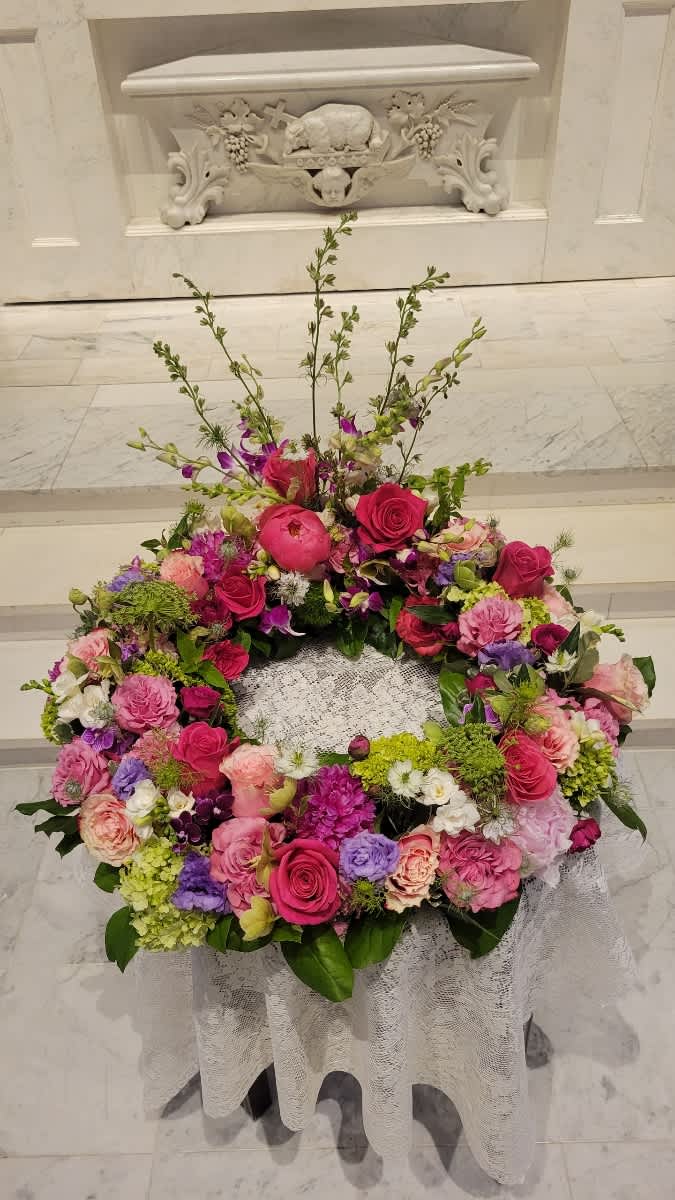Large pink and purple floral wreath on a lace-covered stand