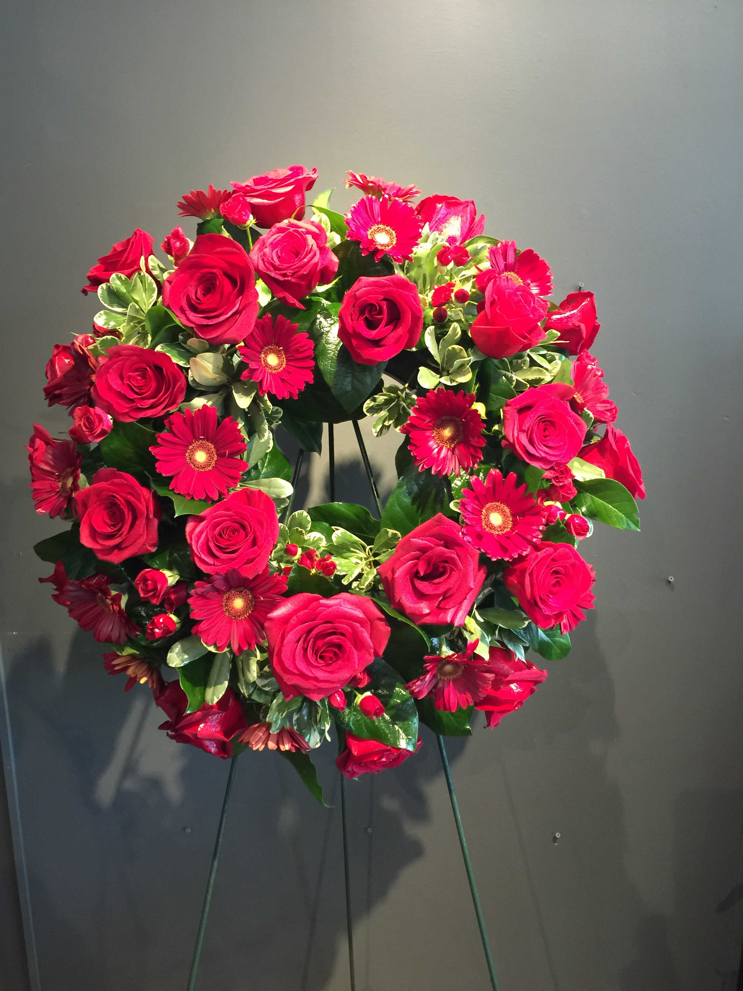 Heart-shaped wreath of red roses and pink daisies on a stand