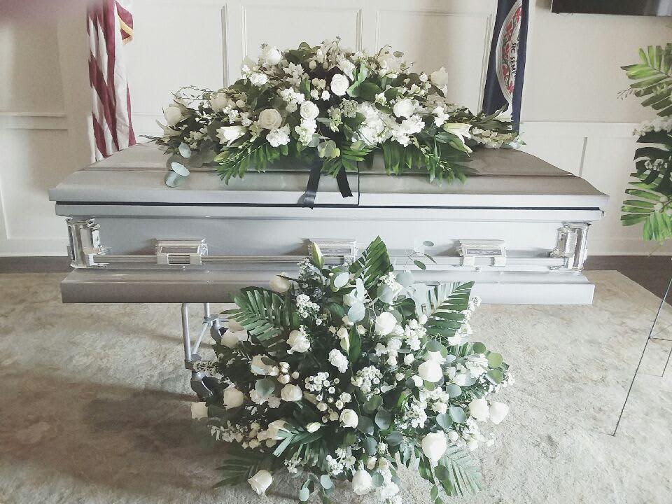 White floral sprays on a silver casket in a funeral setting
