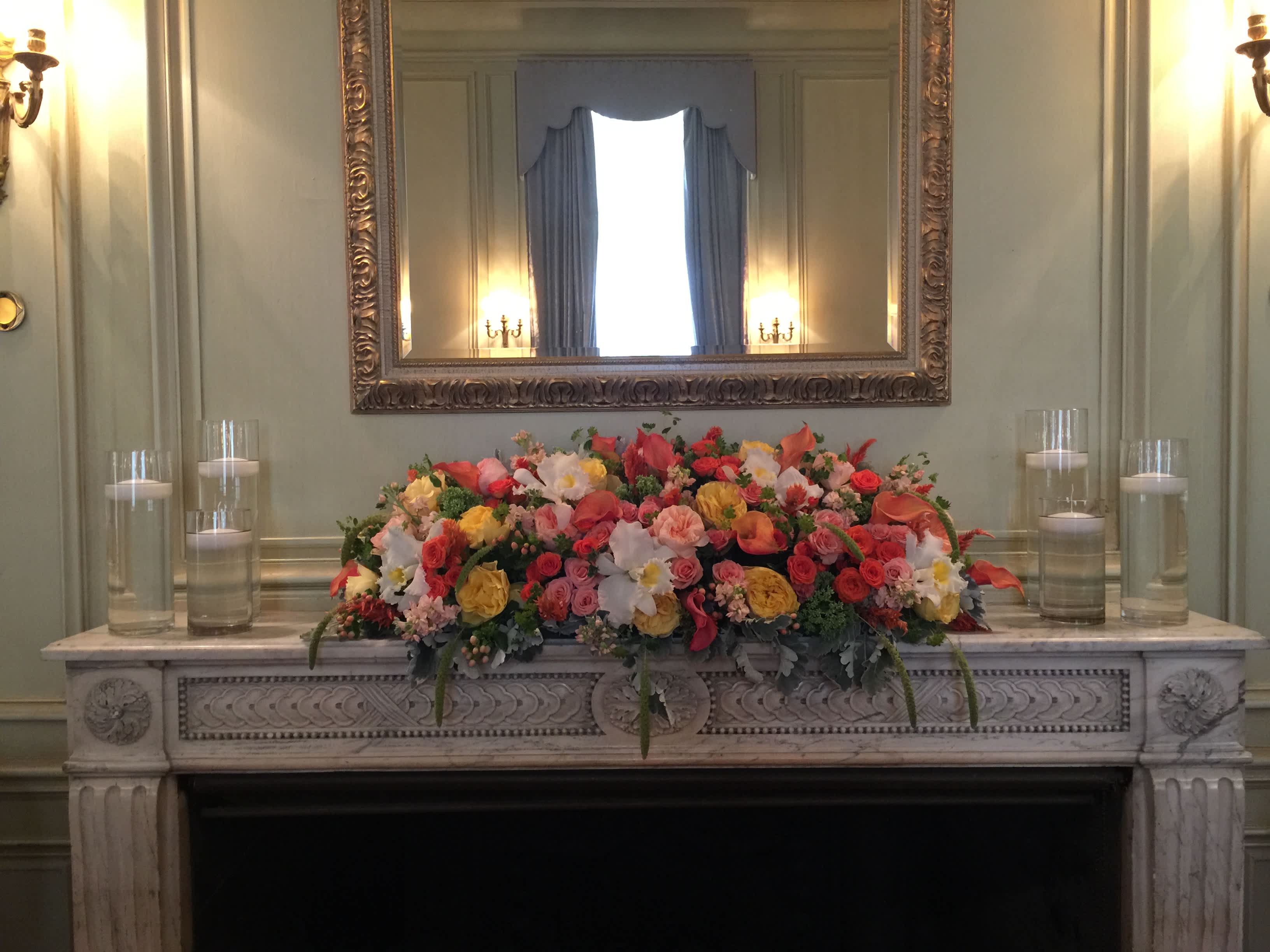 Colorful floral arrangement on a mantel with glass candles on both sides
