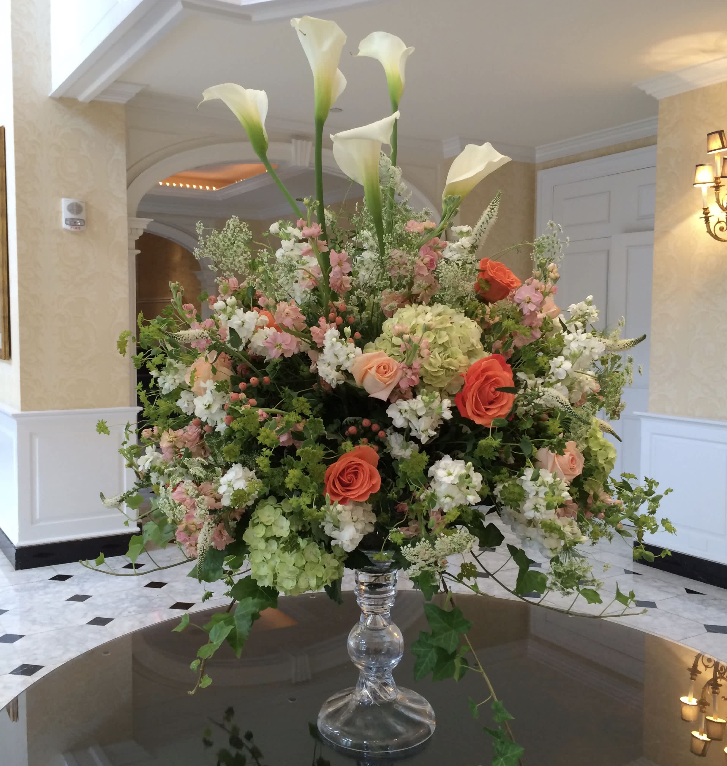 Large floral arrangement with white calla lilies and pink and coral roses in a glass vase