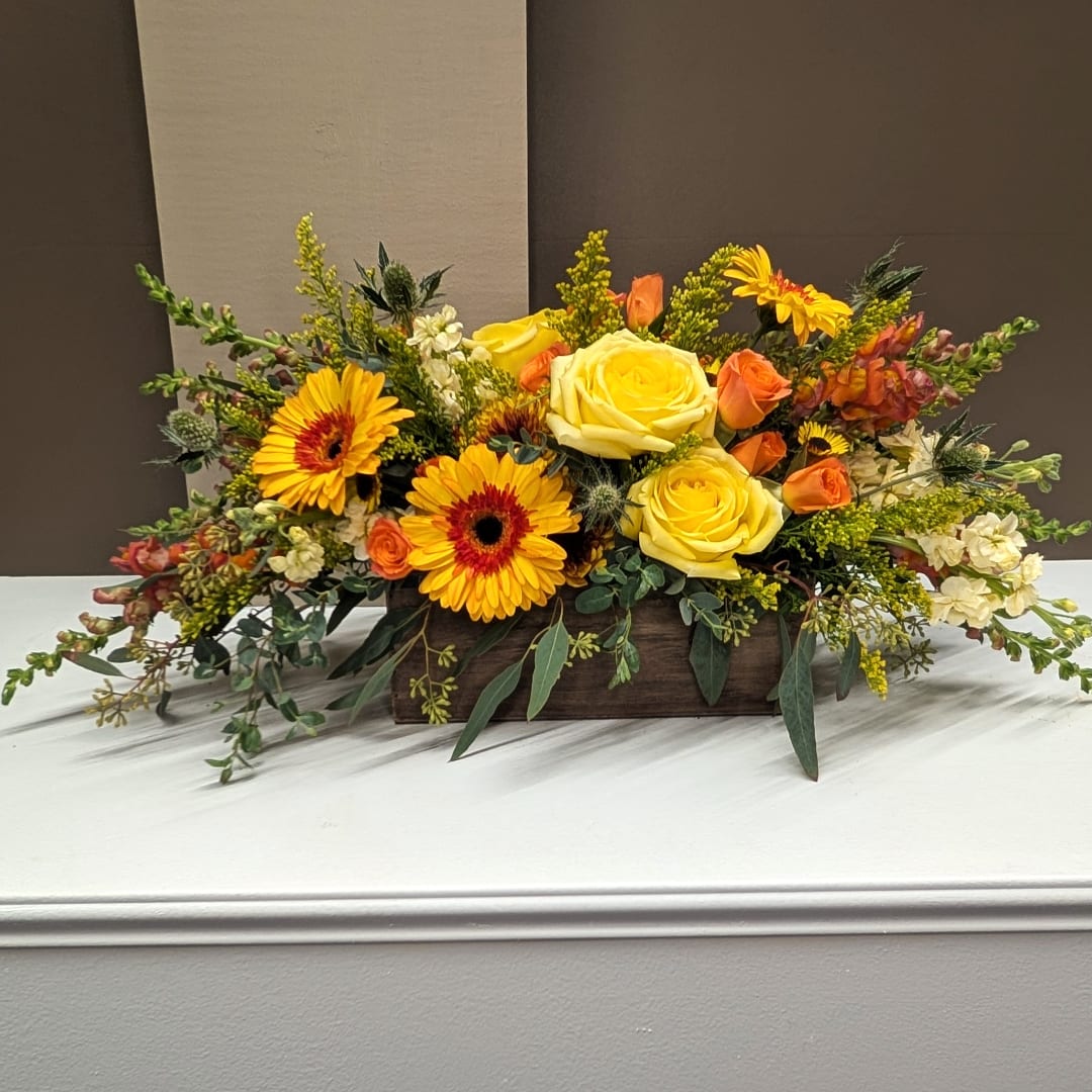 Yellow roses and orange gerbera daisies in a low wooden box
