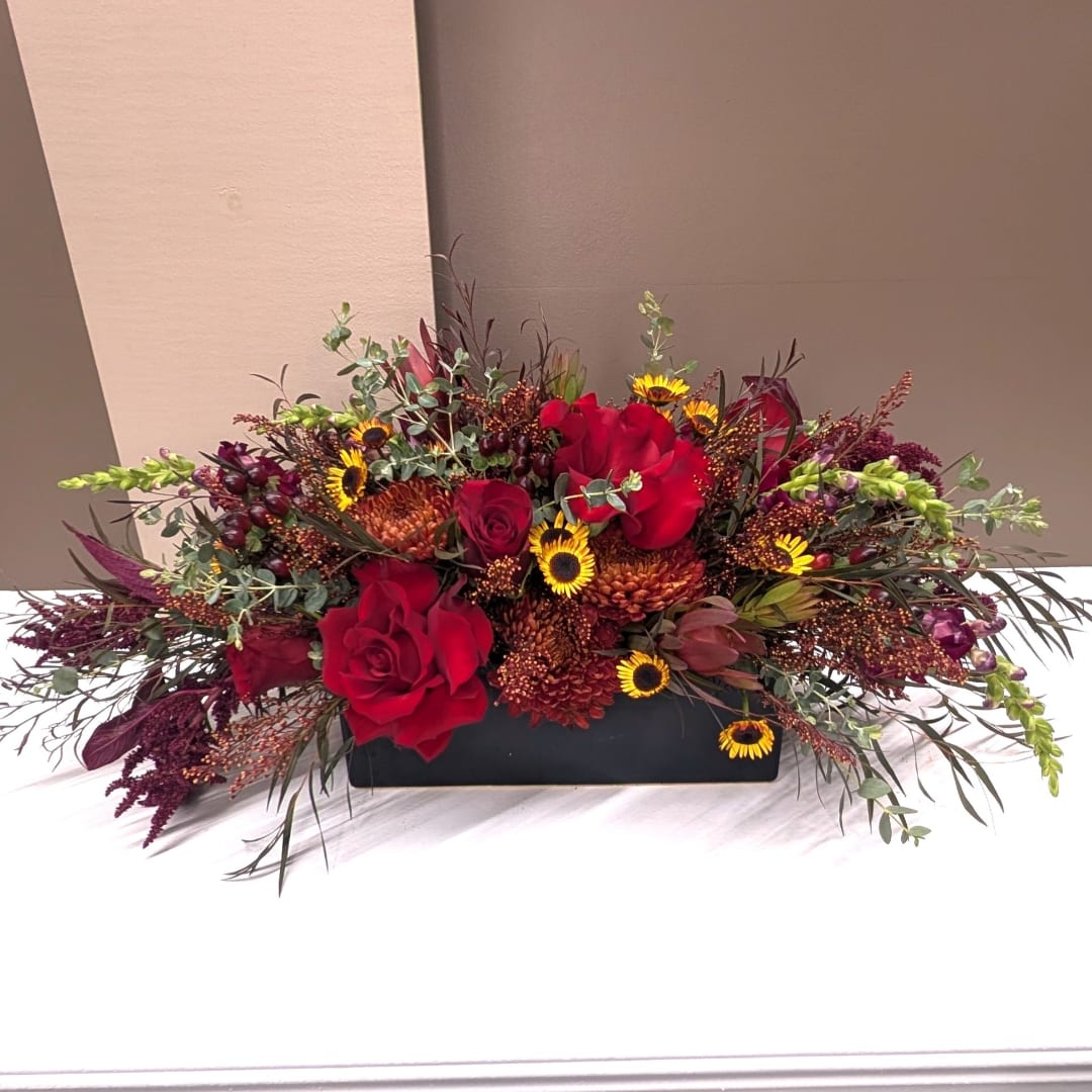 Red roses and small yellow flowers arranged in a low black container