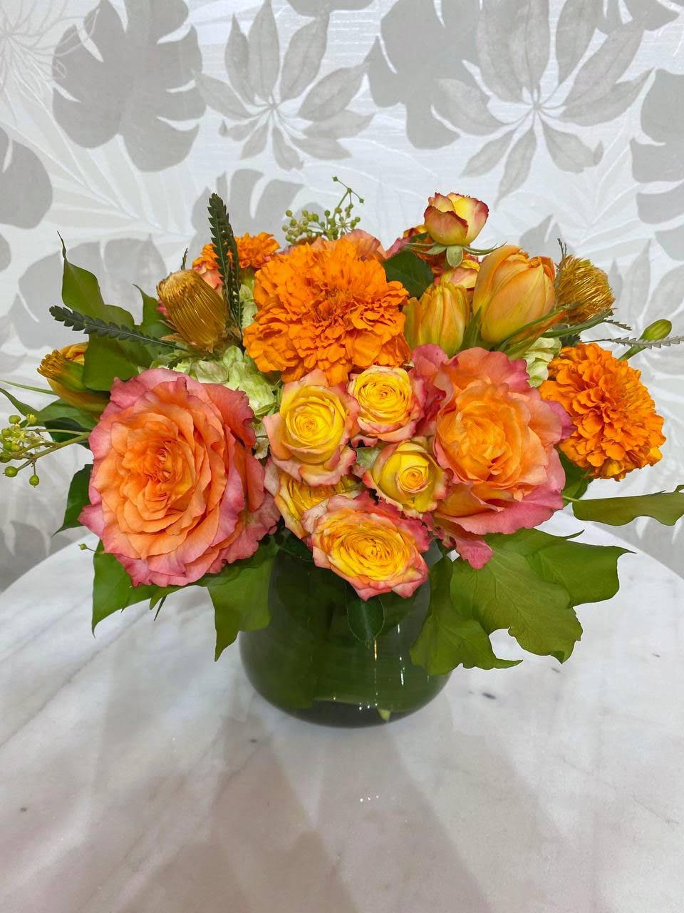 Orange and pink roses with marigolds in a green vase