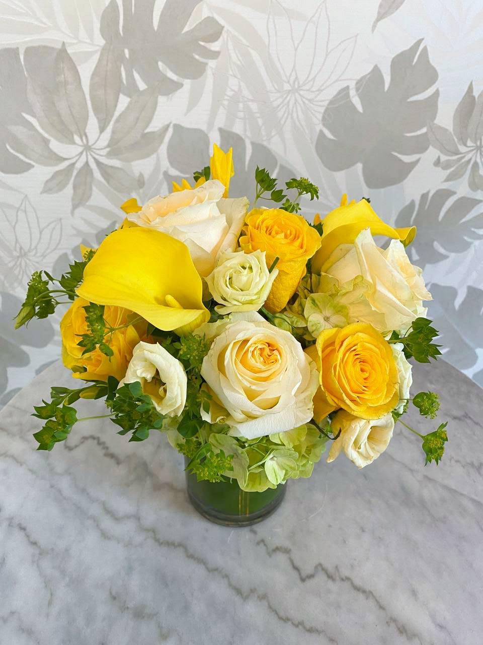 Yellow and white roses with yellow calla lilies in a glass vase