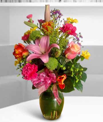 Colorful mixed bouquet in a green glass vase with pink lilies and roses