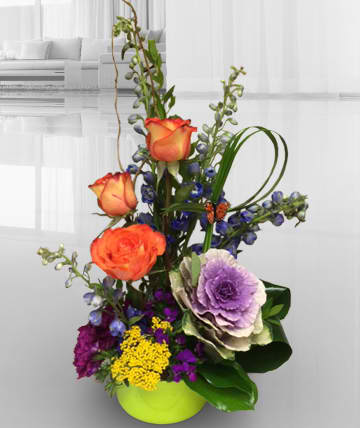 Tall mixed flower arrangement in a lime green vase with orange roses and purple blooms