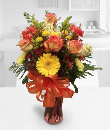 Bouquet of orange roses and yellow gerbera daisies in a vase with a ribbon