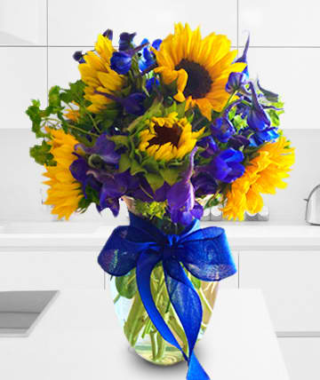 Bouquet of yellow sunflowers and purple flowers in a glass vase with a blue ribbon