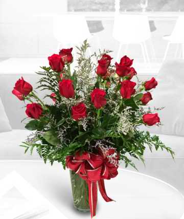 Red roses arranged in a glass vase with a red ribbon