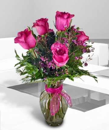Pink roses arranged in a glass vase with a ribbon