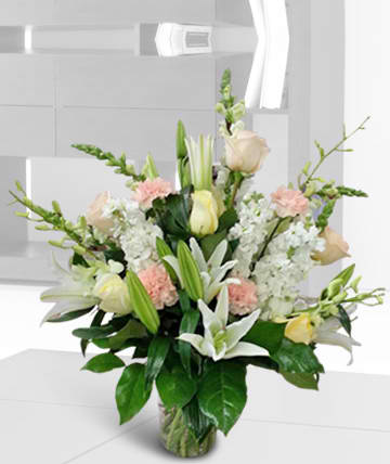Tall bouquet of white lilies, pale roses, and pink carnations in a glass vase