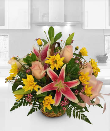 Basket arrangement with pink lilies, yellow daisies, and pale roses