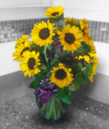 Bouquet of yellow sunflowers in a glass vase with purple ribbon