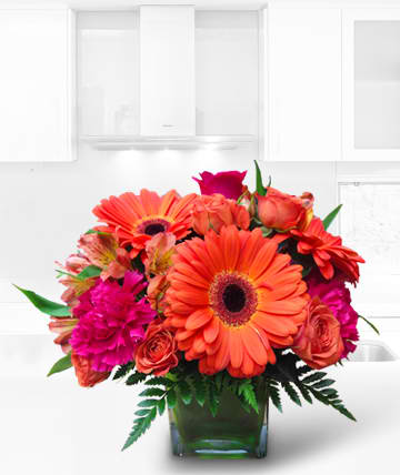 Bright orange and pink mixed bouquet in a square glass vase