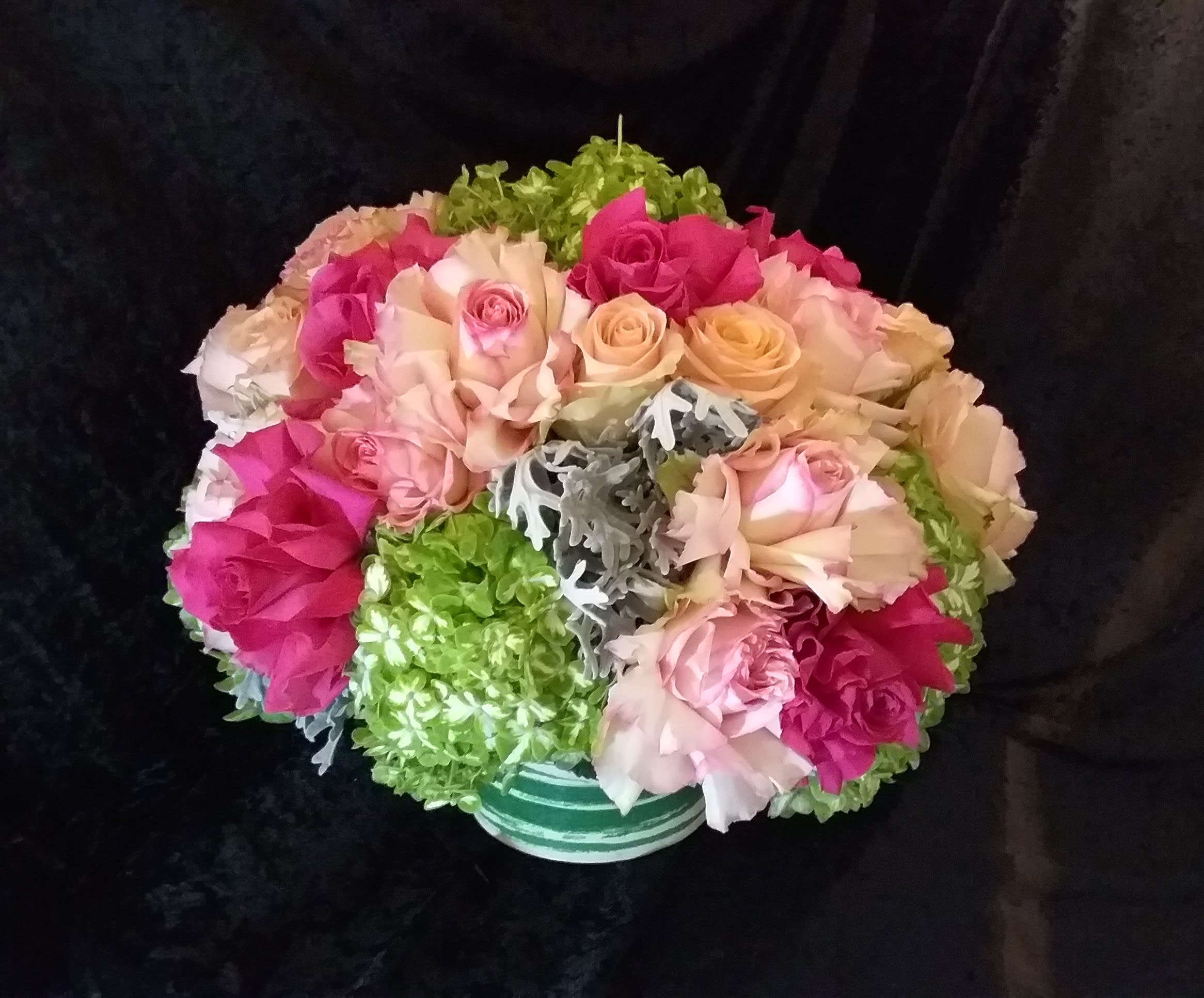 Bouquet of pink and peach roses with green hydrangeas in a striped vase