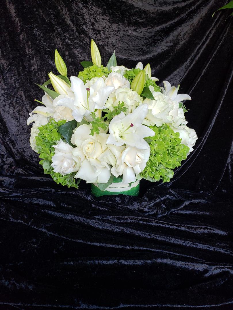 White lilies and roses arranged with green hydrangeas in a low container