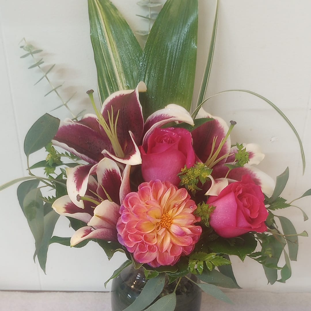Pink roses and a peach dahlia in a glass vase with burgundy lilies