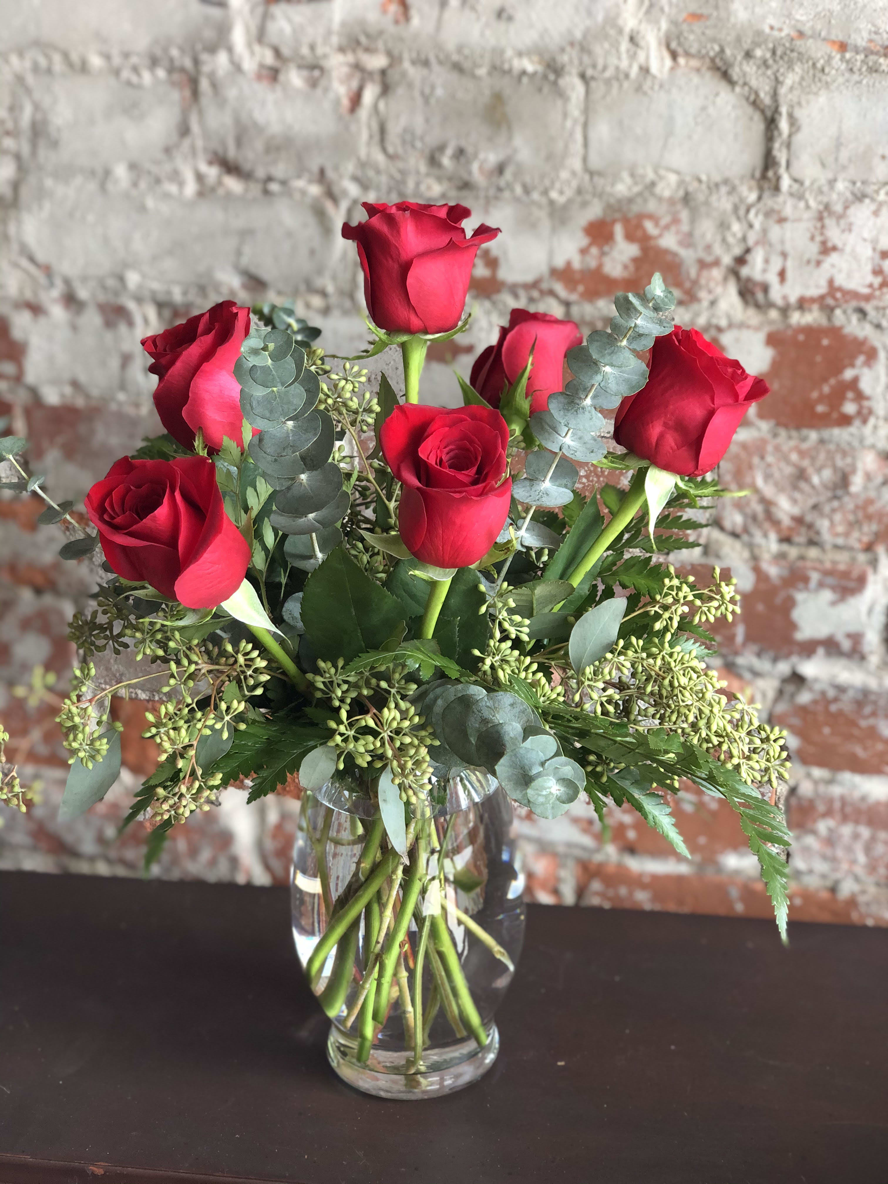 Red roses arranged in a clear glass vase with eucalyptus