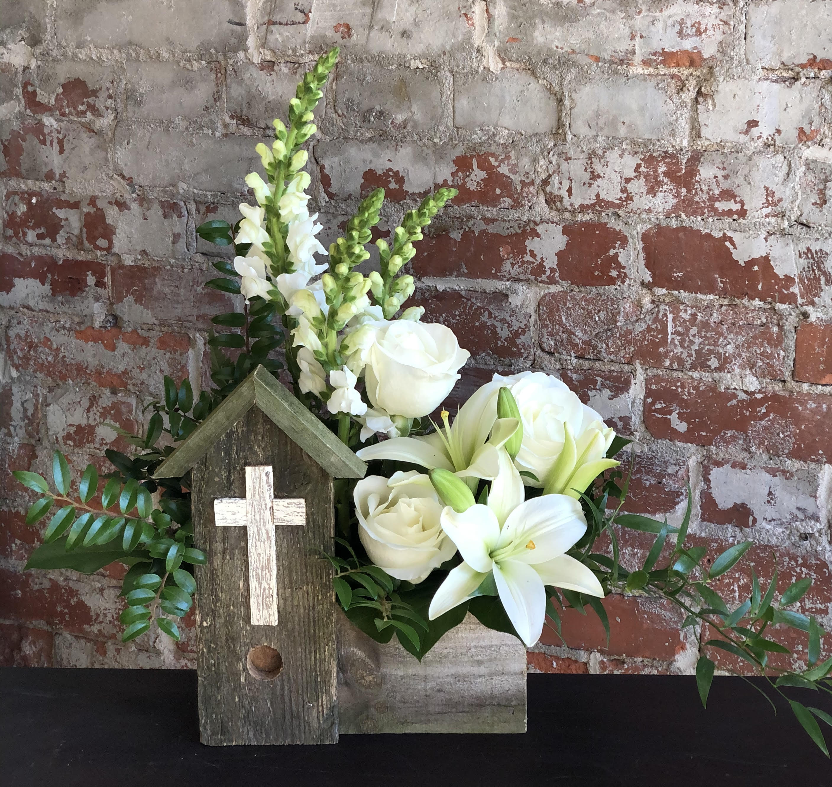 White flowers arranged in a rustic wooden box with a small cross plaque