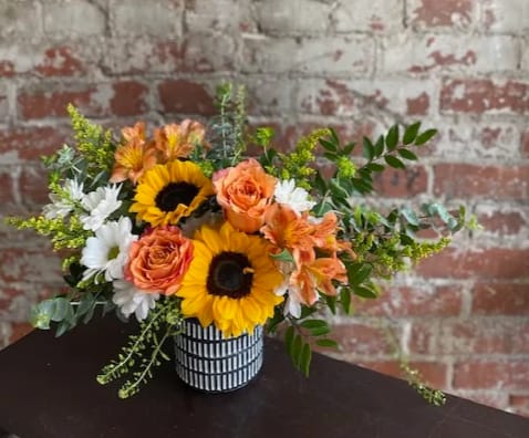 Bouquet of sunflowers, orange roses, and white daisies in a striped vase