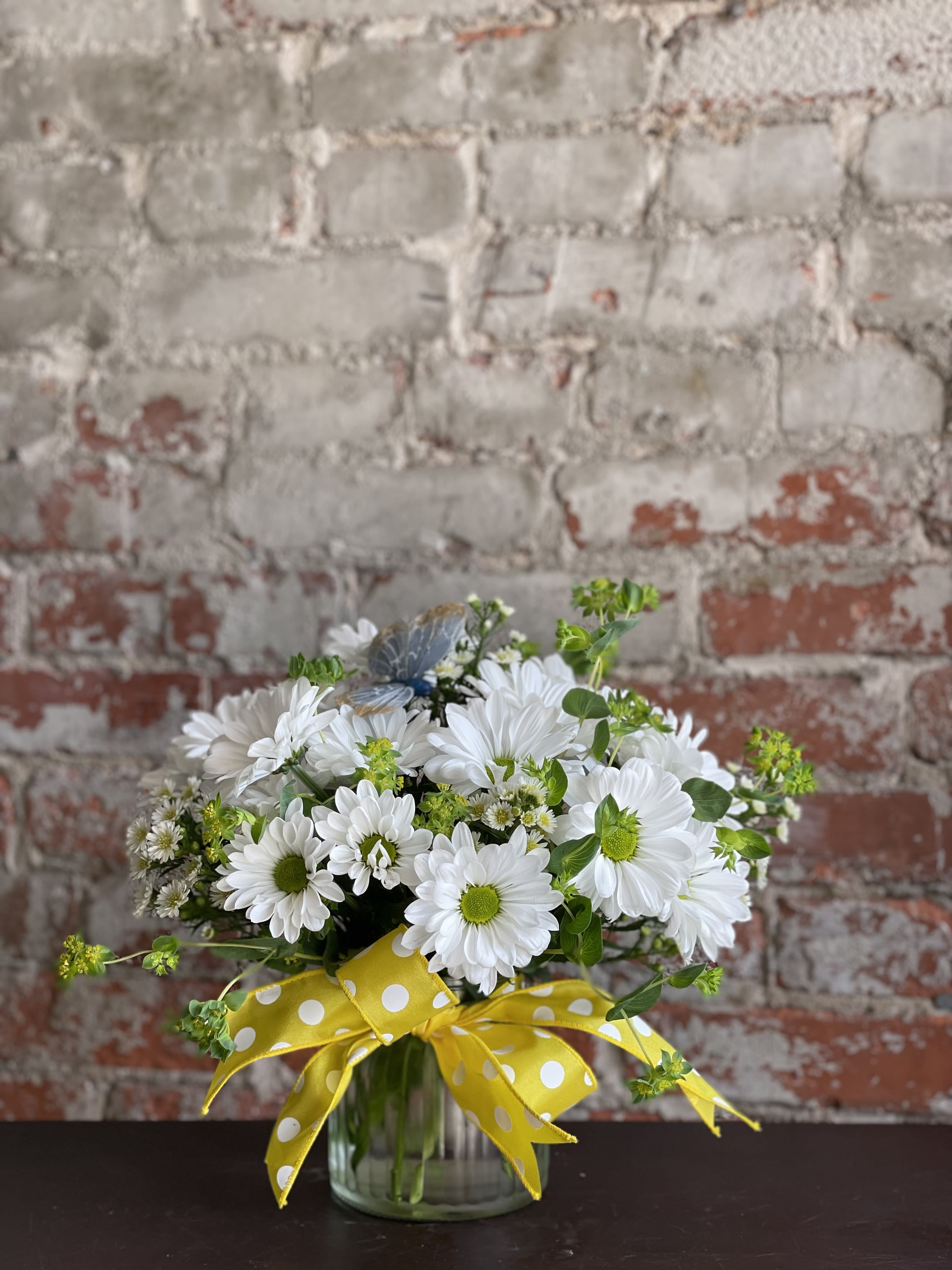 White daisy bouquet in a glass vase with a yellow polka-dot ribbon