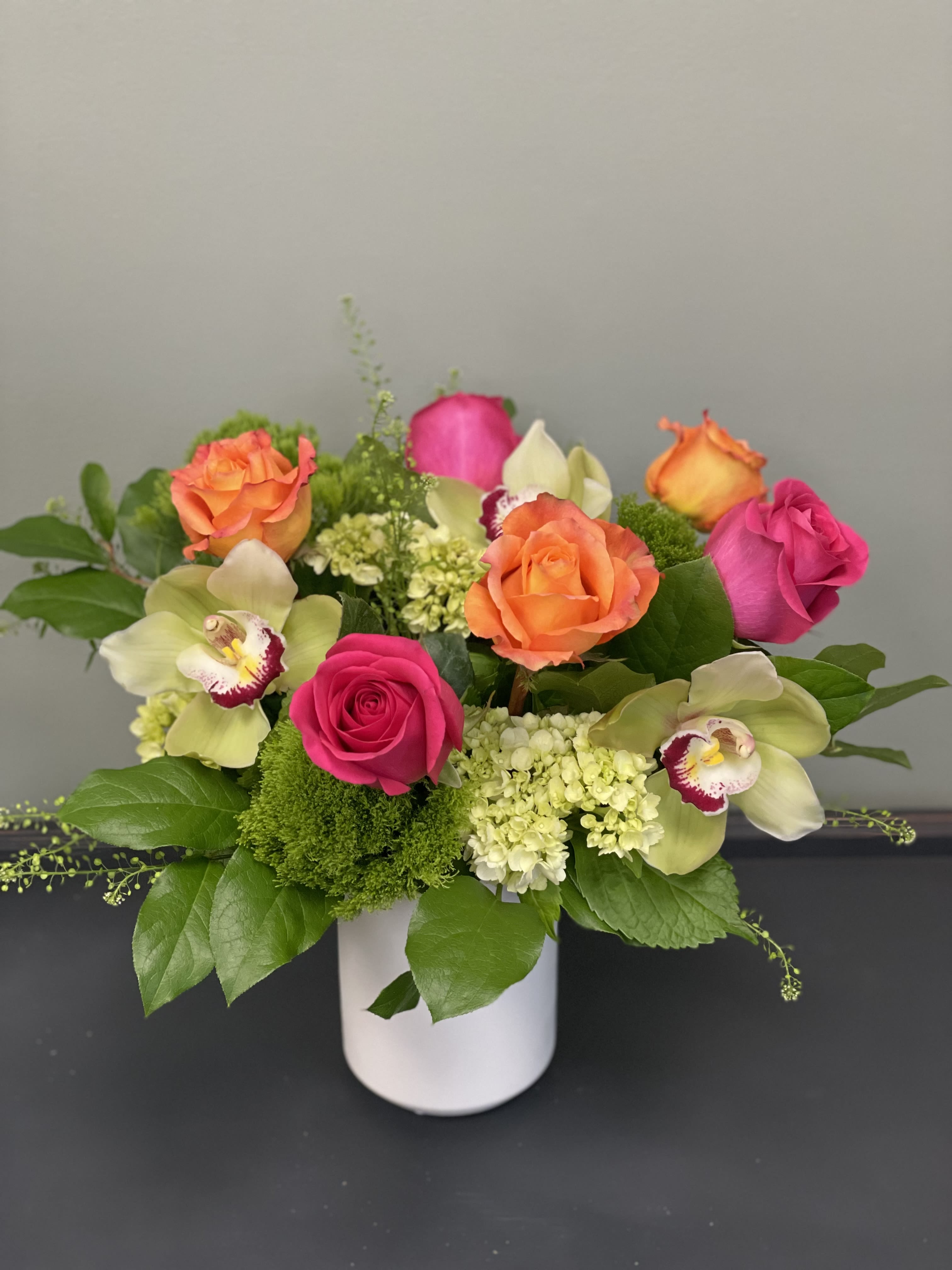 Pink and orange roses with orchids in a white vase