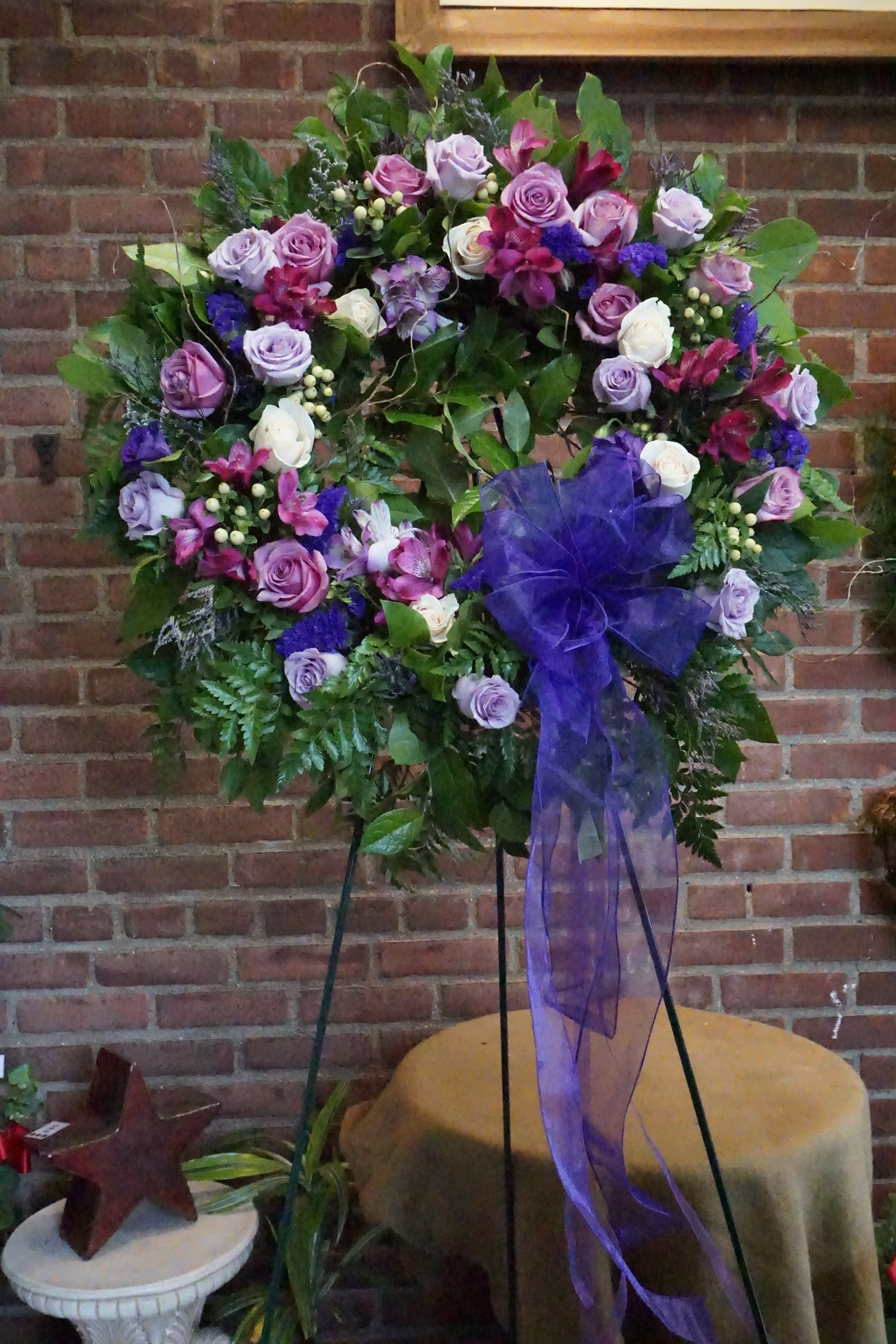 Large floral wreath with purple roses and a sheer purple bow on a stand