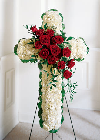 Cross-shaped floral tribute with red roses and white carnations on a stand