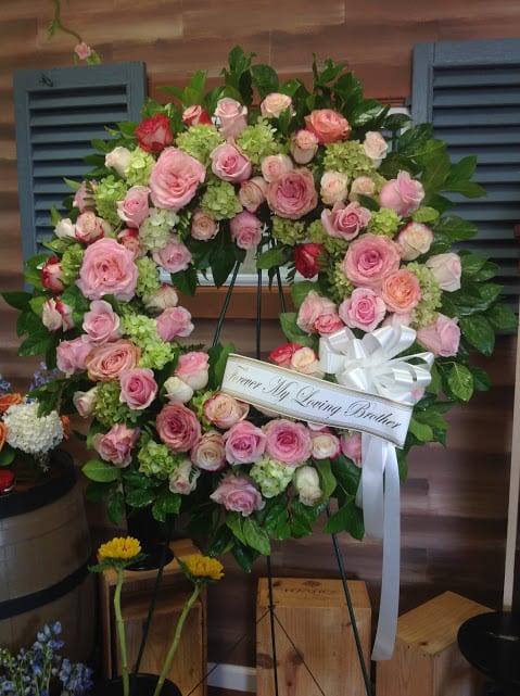 Pink rose funeral wreath with a white ribbon on a stand