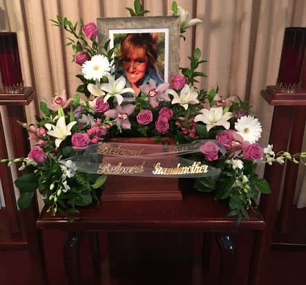 Floral funeral tribute with pink roses, white lilies, and daisies around a framed photo