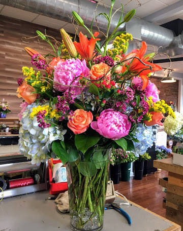 Tall mixed bouquet in a clear glass vase with lilies, roses, peonies, and hydrangeas