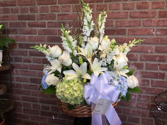 White floral arrangement in a wicker basket with a lavender ribbon