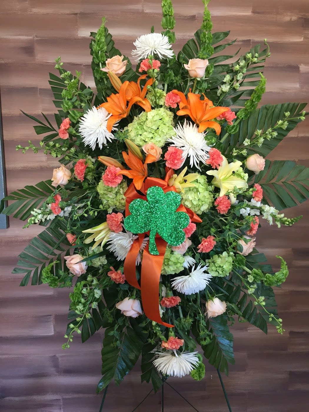 Large floral standing spray with orange lilies and a green shamrock accent