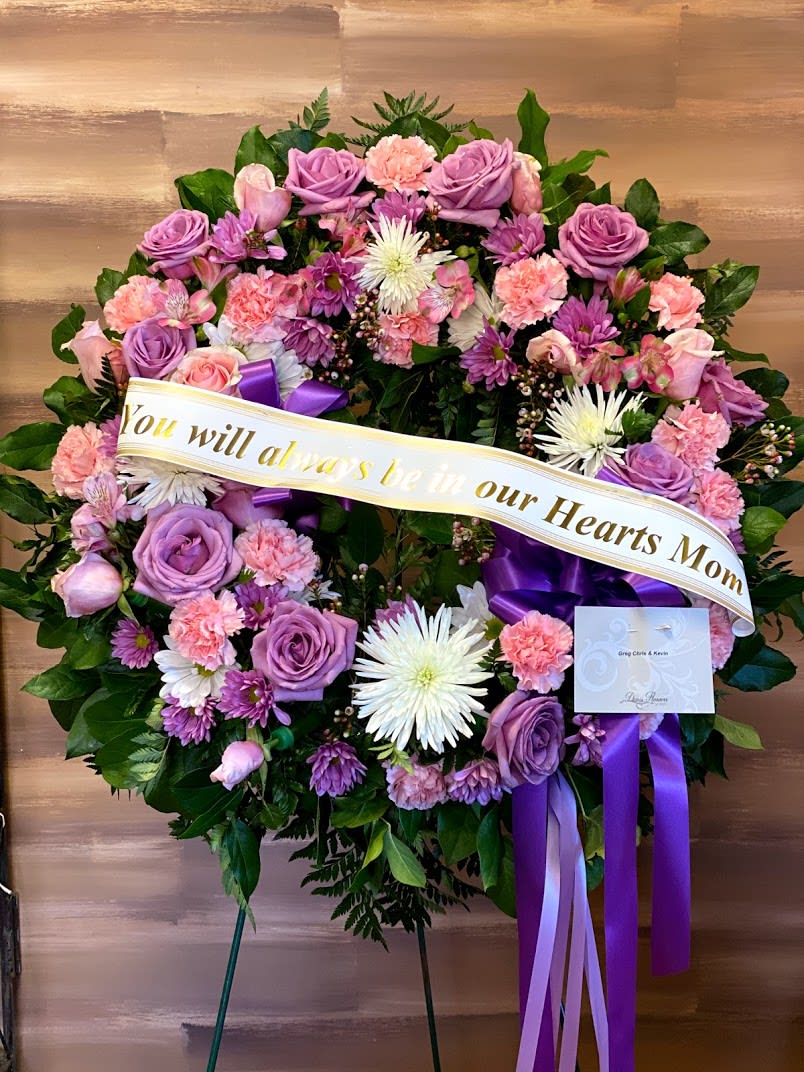 Heart-shaped floral wreath with purple and pink flowers and a memorial ribbon