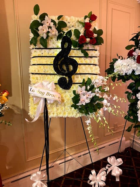 Standing floral tribute with a black treble clef on a white flower panel