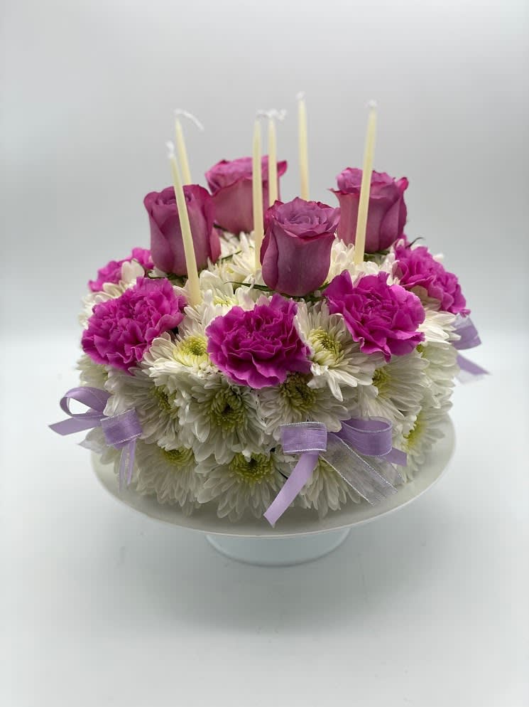 Round floral cake with purple roses and white daisies on a pedestal stand